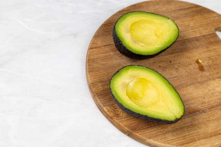 Avocado sliced on half on the cutting wooden board.