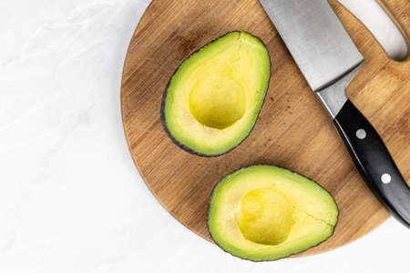 Avocado sliced on half on the wooden board with knife in the background.の写真素材