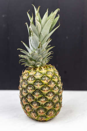 Whole pineapple on the white table with black board background.