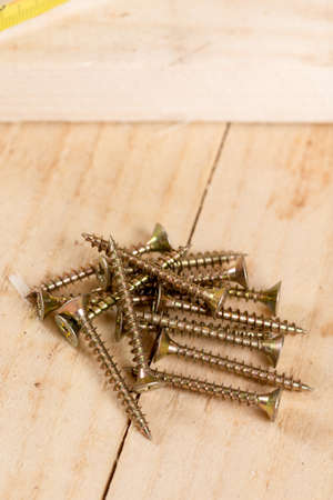 Pile of metar screws on the wooden planks background.