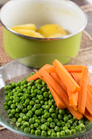 Peeled potatoes with cooked green peas and carrot.の写真素材