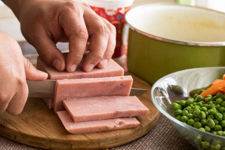 Cook chef slicing ham with ingredients in the background.
