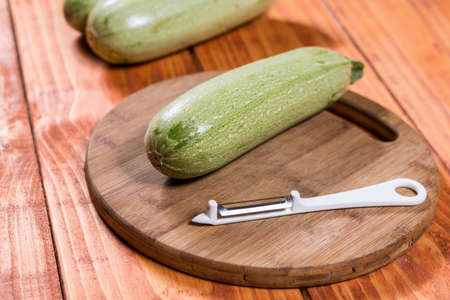 Fresh raw zucchini on the wooden board with knife peeler.の写真素材