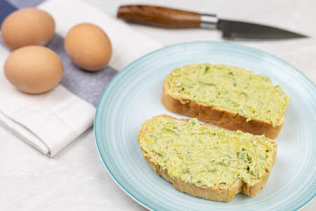 Avocado spread on the toasted bread served on the plate with boiled eggs.