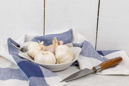 Whole garlic in the white bowl with blue dishcloth and copy space.の写真素材