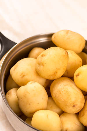 Full pot of young raw potatoes over wooden background.の写真素材