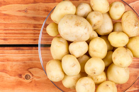 Young raw potatoes in the glass bowl above wooden background.の写真素材