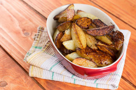 Fried young potatoes in the glass bowl over wooden background.