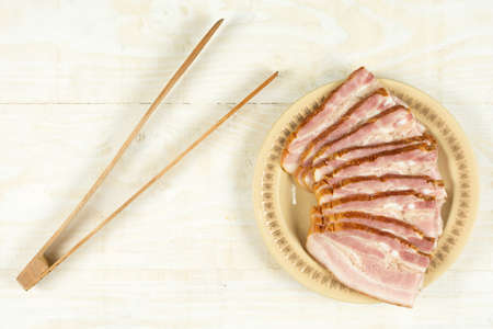 Sliced bacon on the plate above wooden board.