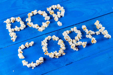 Word popcorn written with pop corns above blue wooden background flat lay.の写真素材