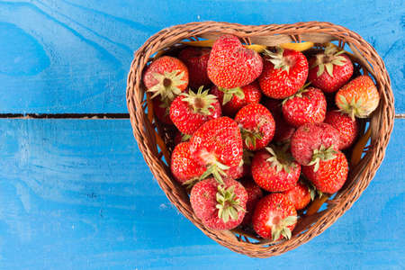 Fresh just picked dirty strawberries in the basket above flat lay of blue wooden backgroundの写真素材