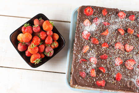 Flat lay chocolate cake with fresh strawberries in the bowl above wooden backgroundの写真素材