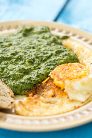 Cooked spinach served with fried eggs and slice of bread.
