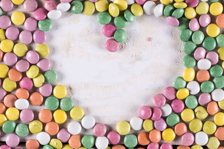 Heart shape above wooden table with colorful round candies arround.