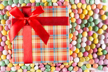 Flat lay box with red bow above colorful round candies.の写真素材