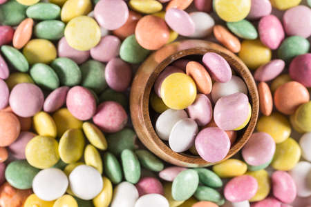 Colorful round candies in the wooden cup.