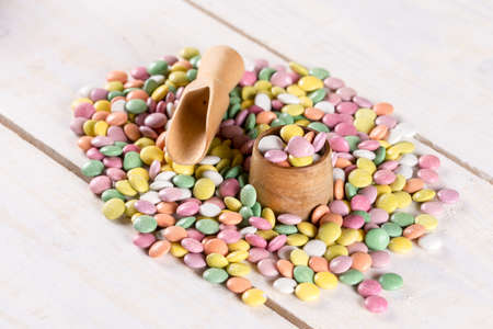 Pile of colorful round candies with wooden cup and spoon.