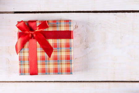 Flat lay above box with red bow and wooden planks background.