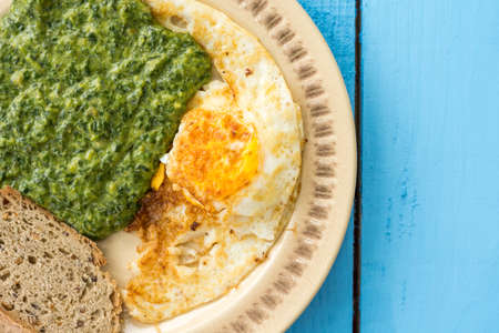 Flat lay spinach with fried eggs and slice of black bread.の写真素材
