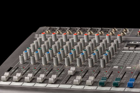 Audio mixing console with knobs and sliders and black background.