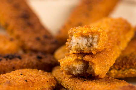 Fried fish meat sticks on the plate above wooden planks table.