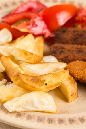 Served meal on the table, fried fish meat sticks with potatoes and tomato salad.