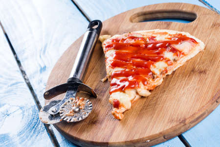 Flat lay above fresh baked pizza triangle slice on the wooden board with cutting knife.