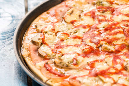 Closeup macro fresh baked round pizza with cheese ham tomato sauce mushrooms.