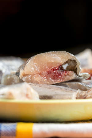 Selective focus on sliced fresh raw hake fish on the green plate.