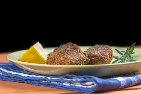 Fried fish on the plate with lemon and rosemary with black background.
