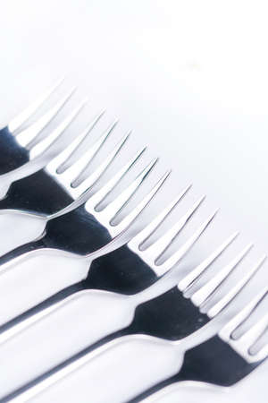 Selective focus closeup macro metal shiny forks lined up over white background.の写真素材