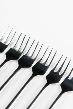 Selective focus closeup macro metal shiny forks lined up over white background.の写真素材