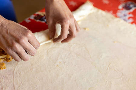 Woman hands rolling raw dough in low key moody light.