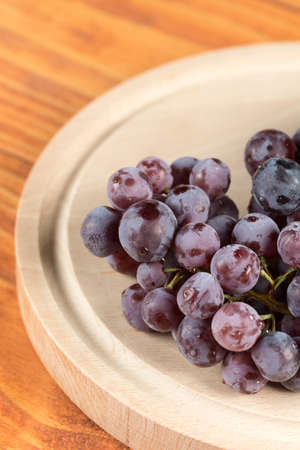 Closeup macro grapes on the round wooden kitchen board on the table.の写真素材