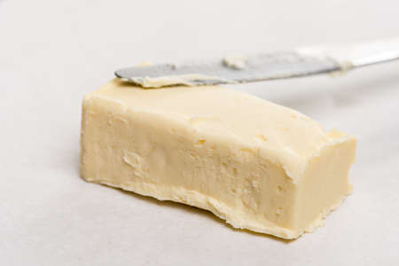 Slice of butter with kitchen knife on the white marble background table.の写真素材