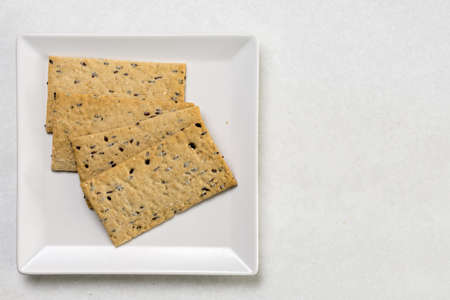 Flax chips on the white square plate above white marble background.の写真素材