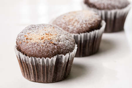 Chocolate brownies cup cakes with powdered sugar on the white marble background.