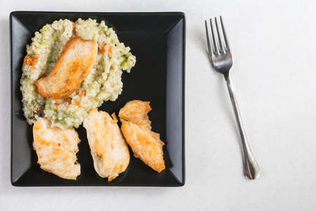 Flat lay above fried chicken white meat with risotto in the black square plate on the white marble.