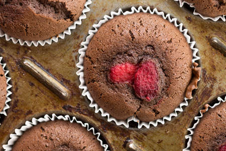 Flat lay above fresh baked chocolate cup cake muffins with raspberries.