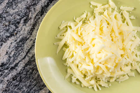 Grated cheese pile on the plate above grey granite background.
