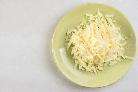 Flat lay above grated cheese on the plate with copy space above white marble.