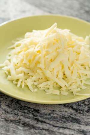 Grated cheese pile on the plate above grey granite background.