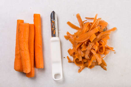 Cleaned and peeled fresh carrot with peeling knife on the white marble table.