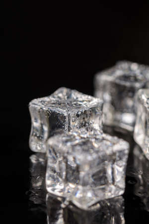 Ice cubes with drops of water on the black background with reflections.