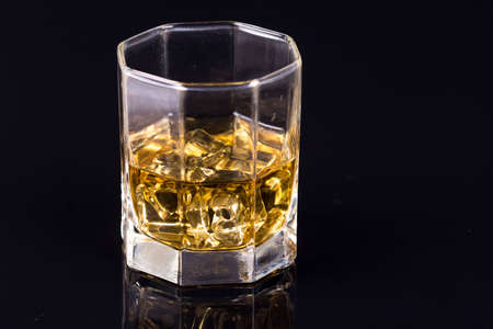 Octagon square glass with whiskey and ice cubes on the black background with reflections.の写真素材