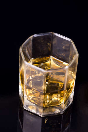 Octagon square glass with whiskey and ice cubes on the black background with reflections.の写真素材