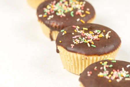 Vanilla cupcakes with chocolate cream and colorful sprinkles isolated on white background.