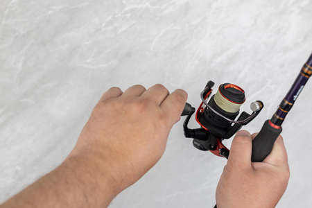 Male hands with fishing rod and fishing reel.