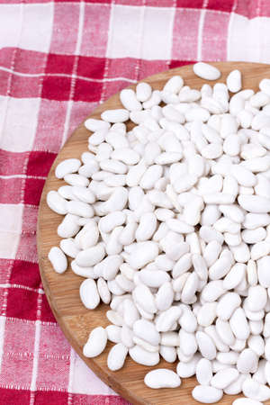 Pile of white beans on the wooden board over table cloth.