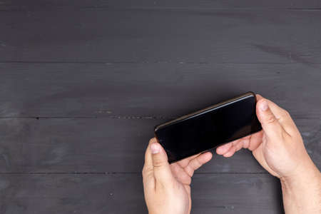 Mobile phone with empty black screen in the male hands above black boards table and copy space.の写真素材
